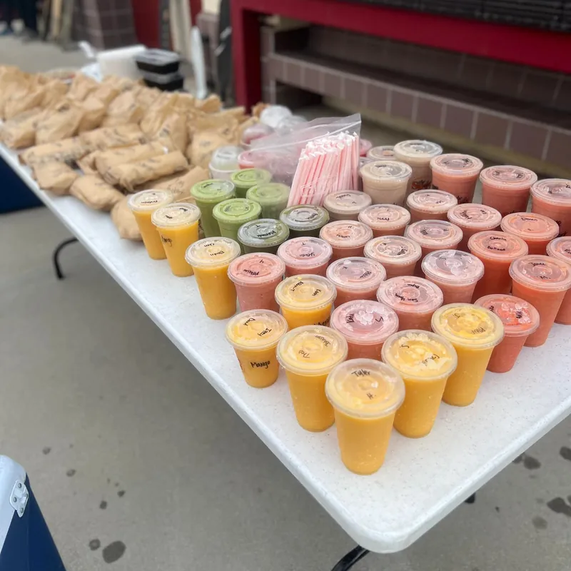 A catering table lined with rows of smoothies and wrapped sandwiches